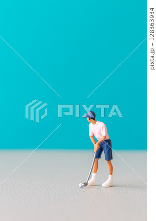 Miniature figurine of a golfer preparing to swing on a vibrant blue background. 128363934
