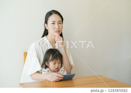 スマートフォンを見る子供と困った表情の母親 スマートフォンを見る子供と困った表情の母親 128365082