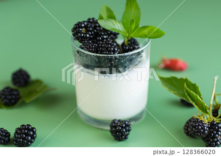 Ripe blackberries with homemade yogurt in a glass on a green background 128366020