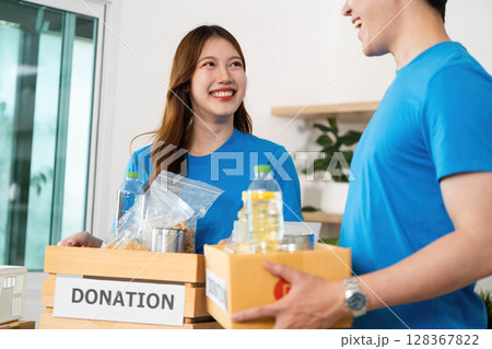 Donation and Community Support. Volunteers packing food items for donation in a cheerful environment. 128367822