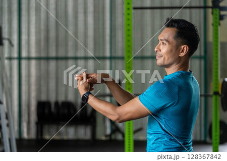 Fitness Stretching Routine. Man performing arm stretches in gym for warm-up. Fitness Stretching Routine. Man performing arm stretches in gym for warm-up. 128367842