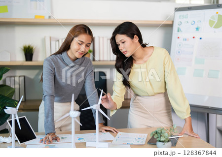 ESG Development. Two women analyzing renewable energy projects in a modern office space. 128367844