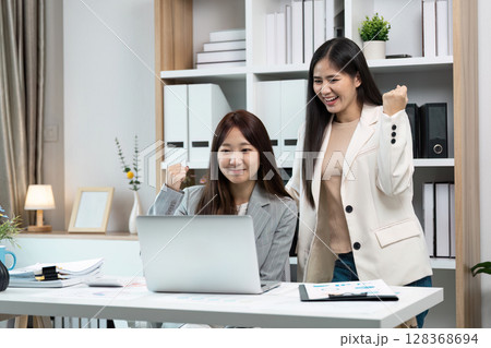 Two Businesswomen Celebrating Success in Modern Office with Laptop and Documents Two Businesswomen Celebrating Success in Modern Office with Laptop and Documents 128368694