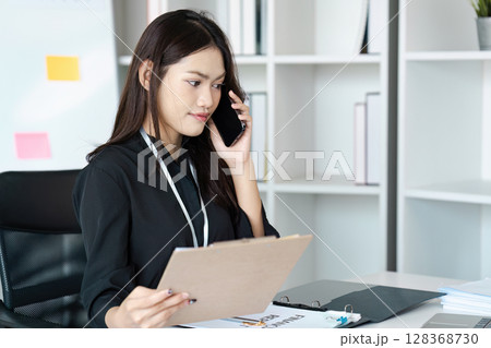 Young Professional Woman in Office on Phone Call Holding Clipboard, Focused on Work 128368730