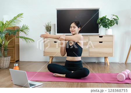 Woman Practicing Yoga at Home on a Pink Mat with Laptop, Promoting Wellness and Healthy Lifestyle in a Modern Living Room Woman Practicing Yoga at Home on a Pink Mat with Laptop, Promoting Wellness and Healthy Lifestyle in a Modern Living Room 128368755
