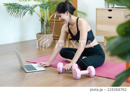 Young Woman Practicing Yoga at Home with Laptop and Dumbbells for a Healthy Lifestyle and Wellness Routine 128368762