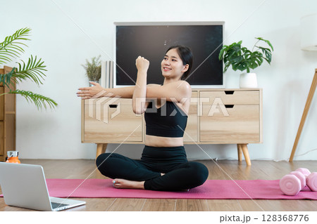 Woman Practicing Yoga at Home on a Pink Mat with Laptop, Promoting Wellness and Healthy Lifestyle in a Modern Living Room 128368776