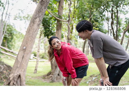 Young Couple Enjoying Outdoor Exercise in a Lush Green Park, Smiling and Staying Hydrated During Their Fitness Routine 128368806