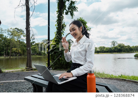 Young Professional Woman Working Remotely Outdoors with Laptop and Water Bottle Near Scenic Lake 128368874