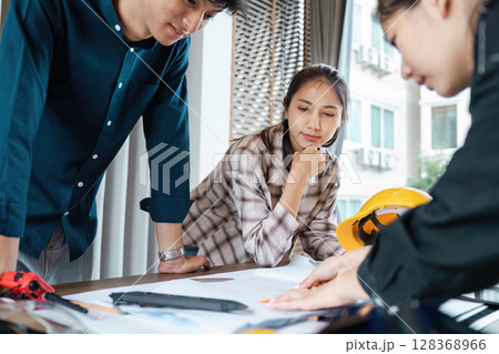 Group of Engineer collaboration on a Project in a Modern Office Setting with Blueprints and Safety Gear 128368966