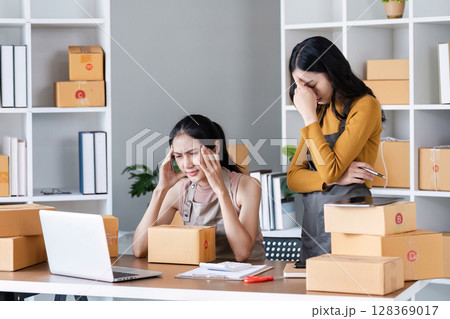 Two stress Business women Managing Online Orders in a Modern Office with Cardboard Boxes and Laptop 128369017