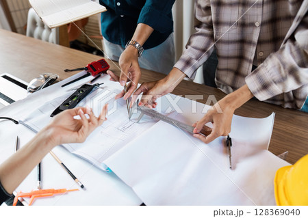 Collaborative Engineers Working on Architectural blueprint and Technical Drawings in Modern Office Setting Collaborative Engineers Working on Architectural blueprint and Technical Drawings in Modern Office Setting 128369040