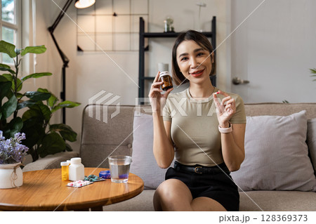 Smiling Woman Holding Pill Bottle and Tablet in Modern Living Room Setting, Promoting Healthcare and Medication 128369373
