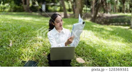 Young Business Woman Digital Nomad Working Outdoors with Laptop and Documents in a Park Setting Young Business Woman Digital Nomad Working Outdoors with Laptop and Documents in a Park Setting 128369381