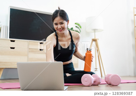 Young Woman Practicing Yoga at Home with Laptop and Dumbbells for a Healthy Lifestyle and Wellness Routine Young Woman Practicing Yoga at Home with Laptop and Dumbbells for a Healthy Lifestyle and Wellness Routine 128369387
