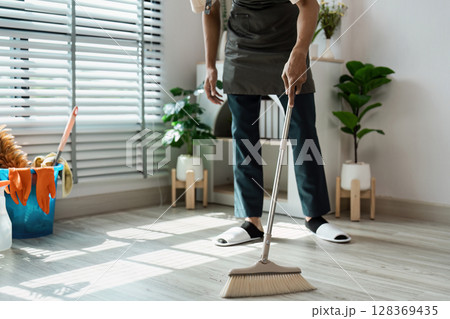 Man Sweeping Floor in Modern Living Room with Plants and Sunlight Through Blinds 128369435