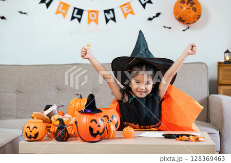Excited Child in Witch Costume Celebrating Halloween with Pumpkins and Decorations Indoors Excited Child in Witch Costume Celebrating Halloween with Pumpkins and Decorations Indoors 128369463