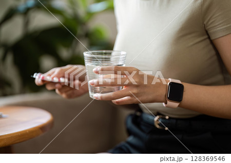 Woman Holding Pills and a Glass of Water for Healthcare and Medication Concept 128369546
