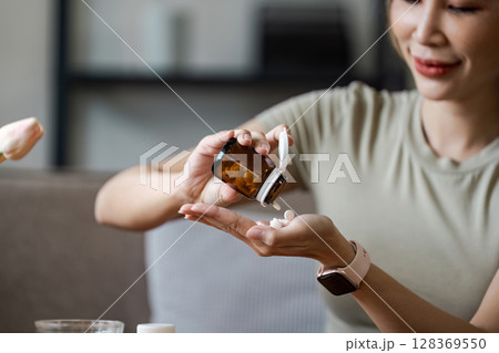 Woman Taking Pills from a Brown Bottle in a Home Setting - Healthcare and Medication Concept Woman Taking Pills from a Brown Bottle in a Home Setting - Healthcare and Medication Concept 128369550