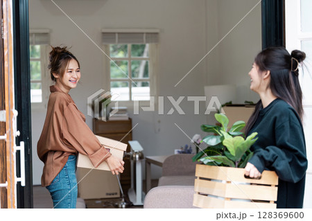 Happy Lesbian Couple Moving into New Home, Carrying Boxes and Plants, Celebrating New Beginnings 128369600