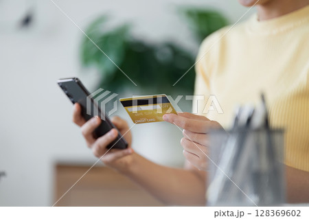 Woman Using Credit Card for Online Shopping on Smartphone in Modern Home Setting Woman Using Credit Card for Online Shopping on Smartphone in Modern Home Setting 128369602