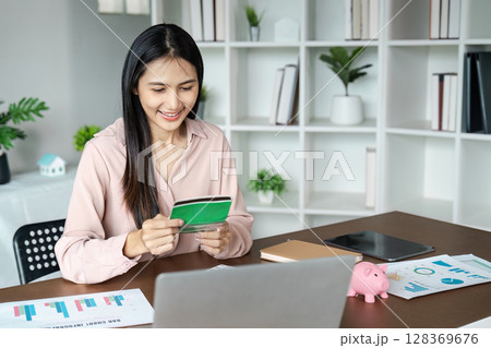 Young Woman Managing Finances at Home with Credit Card, Laptop, and Financial Documents on Desk 128369676