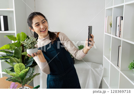 Young Woman Taking Selfie with Potted Plant in Home Office, Showcasing Her Small Business and Gardening Hobby 128369718
