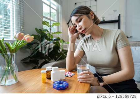 Young Woman Taking Medication at Home, Healthcare Concept with Pills and Water, Modern Living Room Setting 128369729