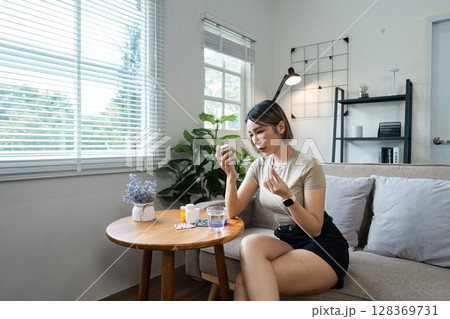 Woman Taking Medication at Home, Healthcare Concept with Pills and Modern Living Room Setting 128369731