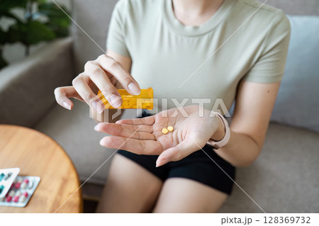 Woman Taking Medication at Home - Healthcare and Wellness Concept with Pills and Prescription Bottle 128369732