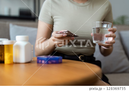 Healthcare at Home: Woman Holding Pills and Glass of Water, Medication Management in a Comfortable Home Setting 128369735