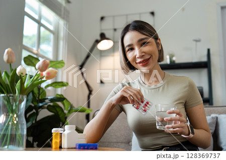 Smiling Woman Taking Medication at Home - Healthcare and Wellness Concept with Pills and Modern Home Interior Smiling Woman Taking Medication at Home - Healthcare and Wellness Concept with Pills and Modern Home Interior 128369737