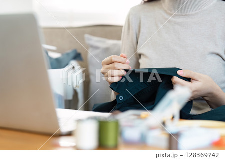 Woman Recycling Clothes at Home by Sewing and Repairing Garments in a Cozy Living Room Setting Woman Recycling Clothes at Home by Sewing and Repairing Garments in a Cozy Living Room Setting 128369742