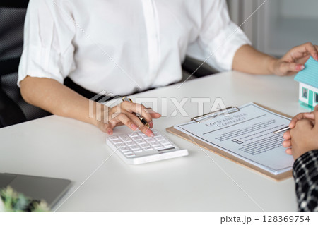 Real Estate Agent Calculating Mortgage Costs with Client, Loan Agreement on Desk Real Estate Agent Calculating Mortgage Costs with Client, Loan Agreement on Desk 128369754