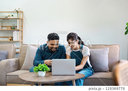 Young Indian Couple Working Together on Laptop at Home, Smiling and Discussing Ideas in a Modern Living Room 128369778
