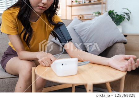 Young Woman Measuring Blood Pressure at Home Using Digital Monitor for Healthcare and Wellness Young Woman Measuring Blood Pressure at Home Using Digital Monitor for Healthcare and Wellness 128369829