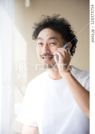 明るい日差しの中スマホで通話をする髭の男性 明るい日差しの中スマホで通話をする髭の男性 128373754