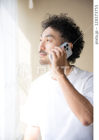 明るい日差しの中スマホで通話をする髭の男性の横顔 明るい日差しの中スマホで通話をする髭の男性の横顔 128373755
