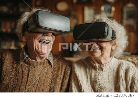 Elderly couple sharing joyful moment wearing virtual reality headsets together in cozy sweaters at home 128376367
