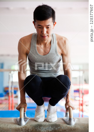 Young man performing gymnastic elements on pommel horse 128377607