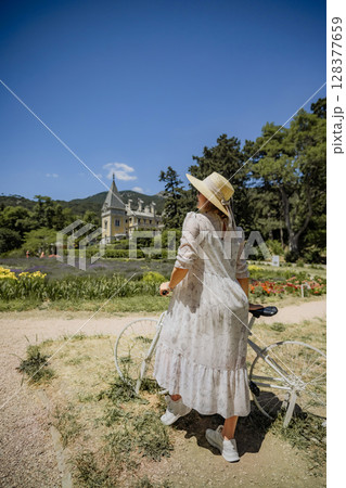 A woman in a white dress is riding a bicycle in a field A woman in a white dress is riding a bicycle in a field 128377659