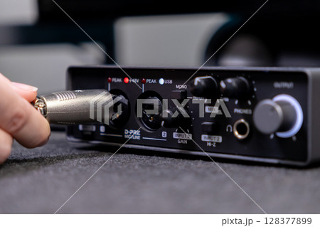 A person's hand inserting an XLR audio cable into a black digital interface, crucial for high-quality sound recording, podcasting, and music production A person's hand inserting an XLR audio cable into a black digital interface, crucial for high-quality sound recording, podcasting, and music production 128377899