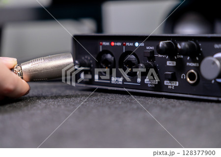 Hand connecting an XLR cable to a compact black audio interface, essential equipment for professional sound recording, music production, and podcasting Hand connecting an XLR cable to a compact black audio interface, essential equipment for professional sound recording, music production, and podcasting 128377900