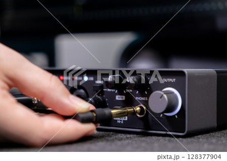 A person's hand plugs a jack cable into the PHONES output of a professional audio interface, essential for music production and sound engineering A person's hand plugs a jack cable into the PHONES output of a professional audio interface, essential for music production and sound engineering 128377904