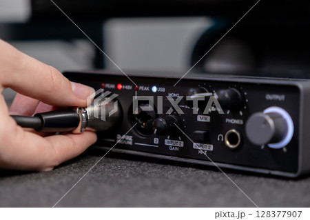 Close-up of a hand inserting an XLR microphone cable into a professional audio interface, highlighting input gain and USB indicators for home studio recording 128377907