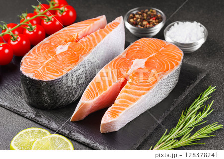Two fresh raw salmon steaks with tomatoes, spices, rosemary and lime on black stone background 128378241