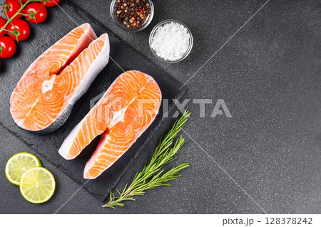 Two fresh raw salmon steaks with tomatoes, spices, rosemary and lime on black stone background Two fresh raw salmon steaks with tomatoes, spices, rosemary and lime on black stone background 128378242
