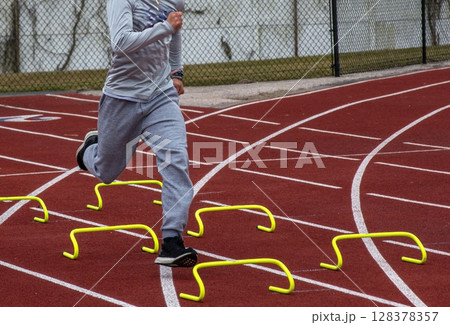 Athlete Training Over MiniHurdles on Outdoor Track in Springtime Athlete Training Over MiniHurdles on Outdoor Track in Springtime 128378357