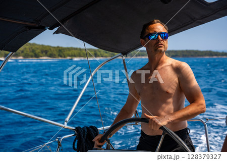 Man with bare torso steering a yacht on the open sea on a sunny day. Concept: summer vacation, yachting, sea travel. 128379327