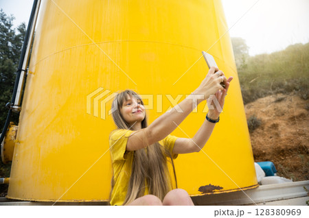 Woman Taking a Selfie in Front of a Bright Yellow Tank in a Natural Setting Woman Taking a Selfie in Front of a Bright Yellow Tank in a Natural Setting 128380969